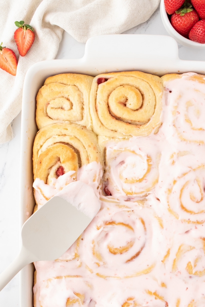 Side view of a pan of strawberry sweet rolls halfway glazed, showing contrast between frosted and unfrosted.