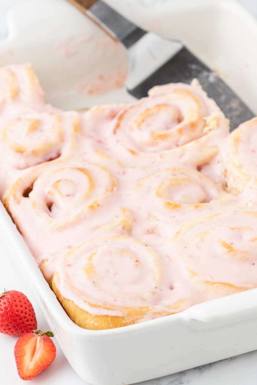 Lifting a warm strawberry sweet roll out of the pan with an offset spatula.