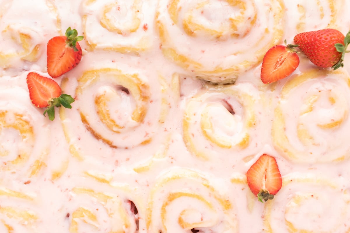 Close-up shot of glazed strawberry sweet rolls highlighting the glossy glaze and textured swirl.