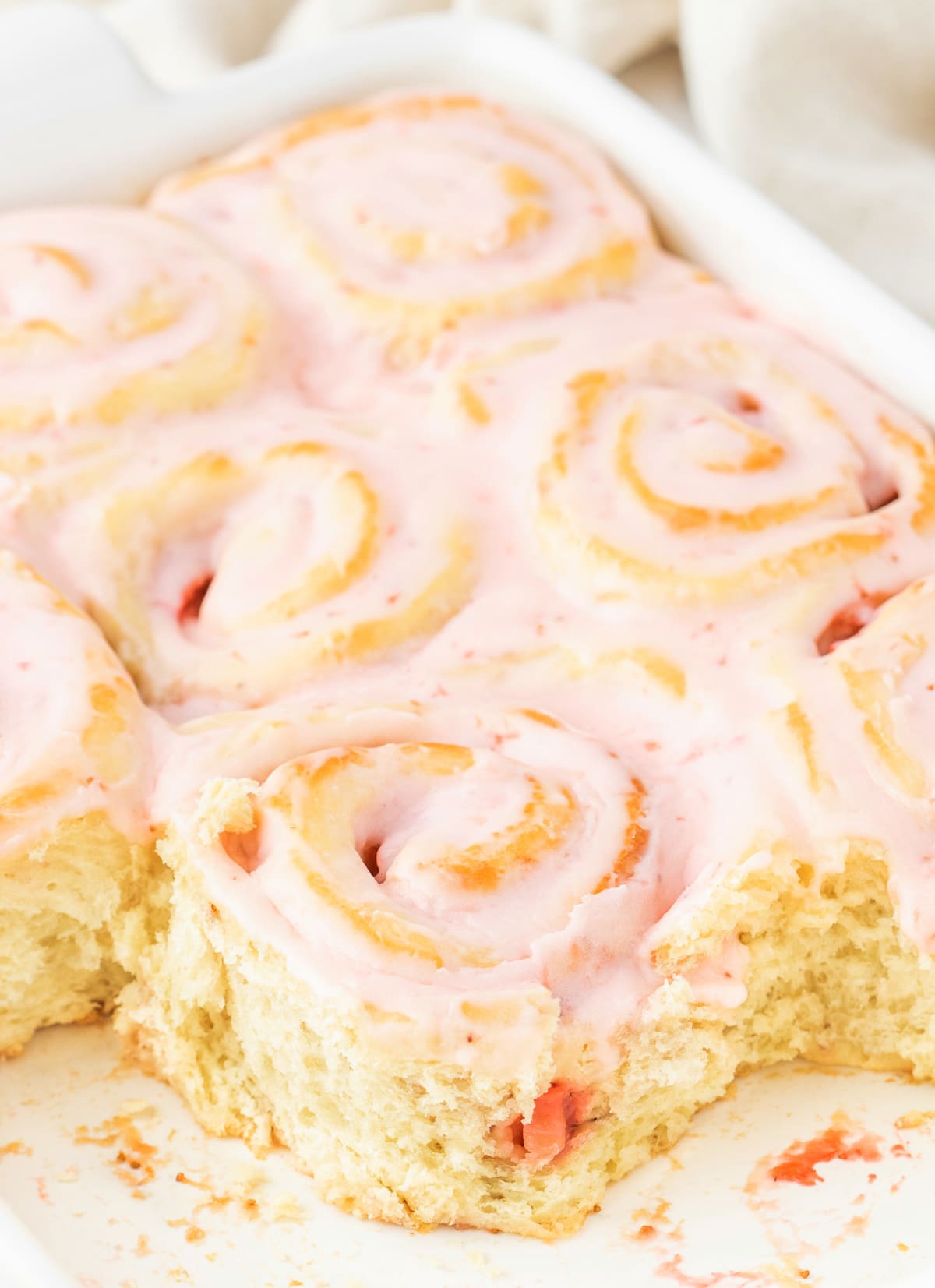Overhead view of a pan of baked strawberry sweet rolls with a few removed, showing the soft, jammy centers.