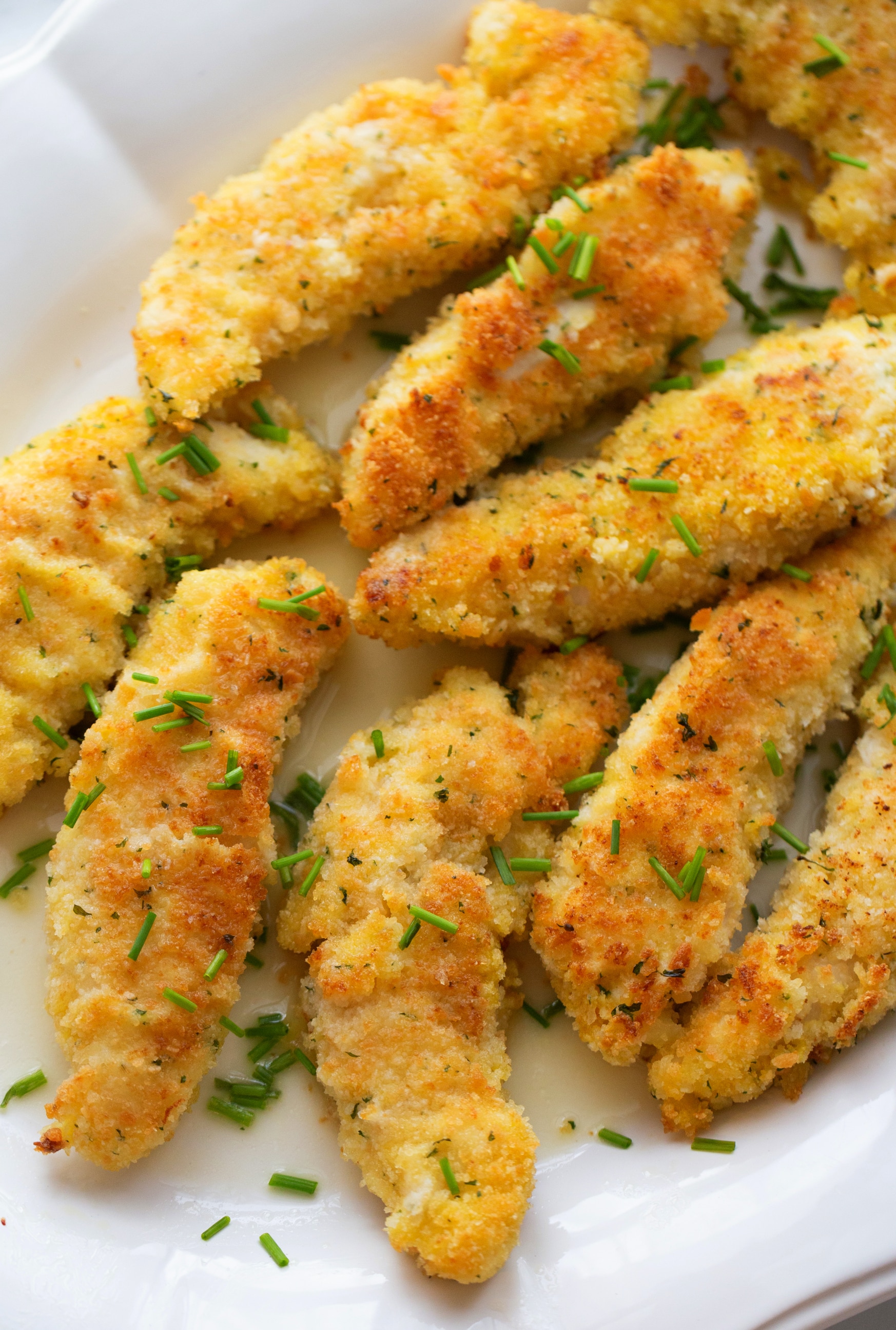 Chicken Tenderloin Piccata on a platter Golden, crispy chicken tenderloin piccata served on a white platter, drizzled with a tangy lemon-butter sauce and topped with fresh chives.