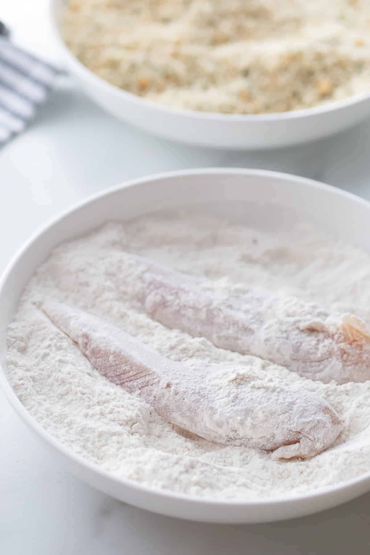 Chicken Tenderloin Piccata being dredged in flour A raw chicken tenderloin being coated in a seasoned flour mixture, the first step in the breading process.