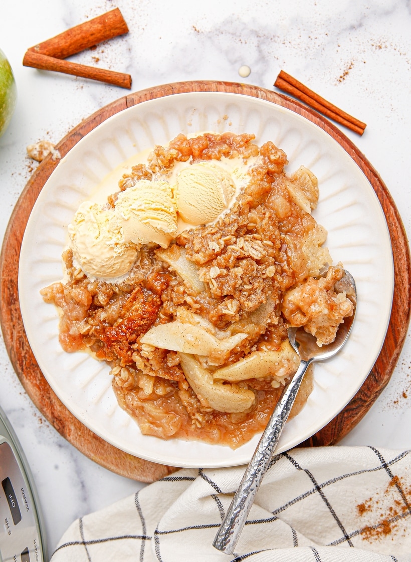 A plate of crockpot apple crisp topped with vanilla ice cream, showing the crunchy oat topping and tender apples.