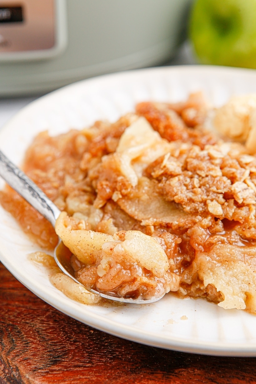 Crockpot apple crisp on a plate with a spoonful ready to serve, topped with crunchy oats and cinnamon apples.