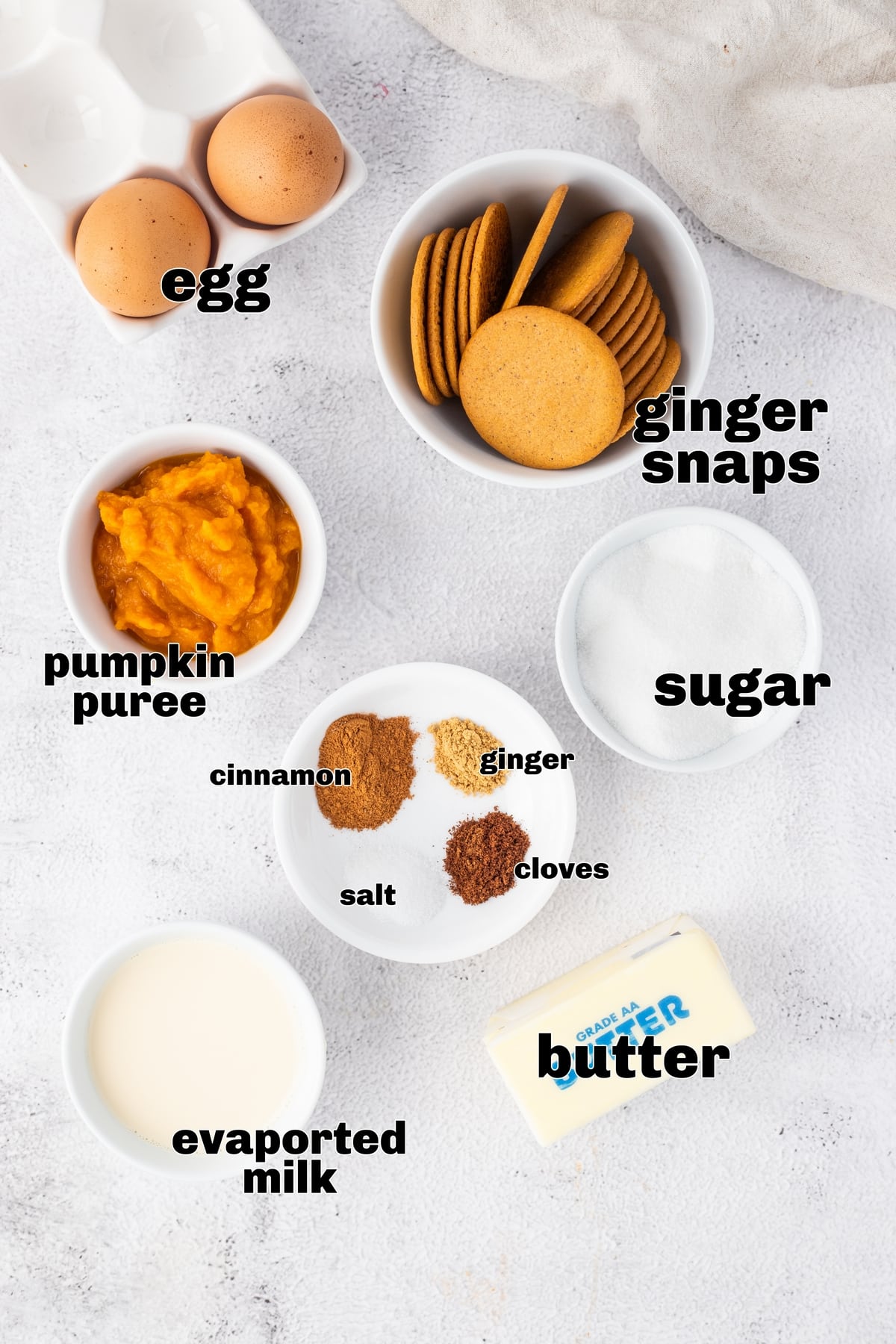 Bowls of ingredients for pumpkin tart filling including pumpkin purée, gingersnap cookies, butter, sugar, spices, egg, and evaporated milk on a white surface.