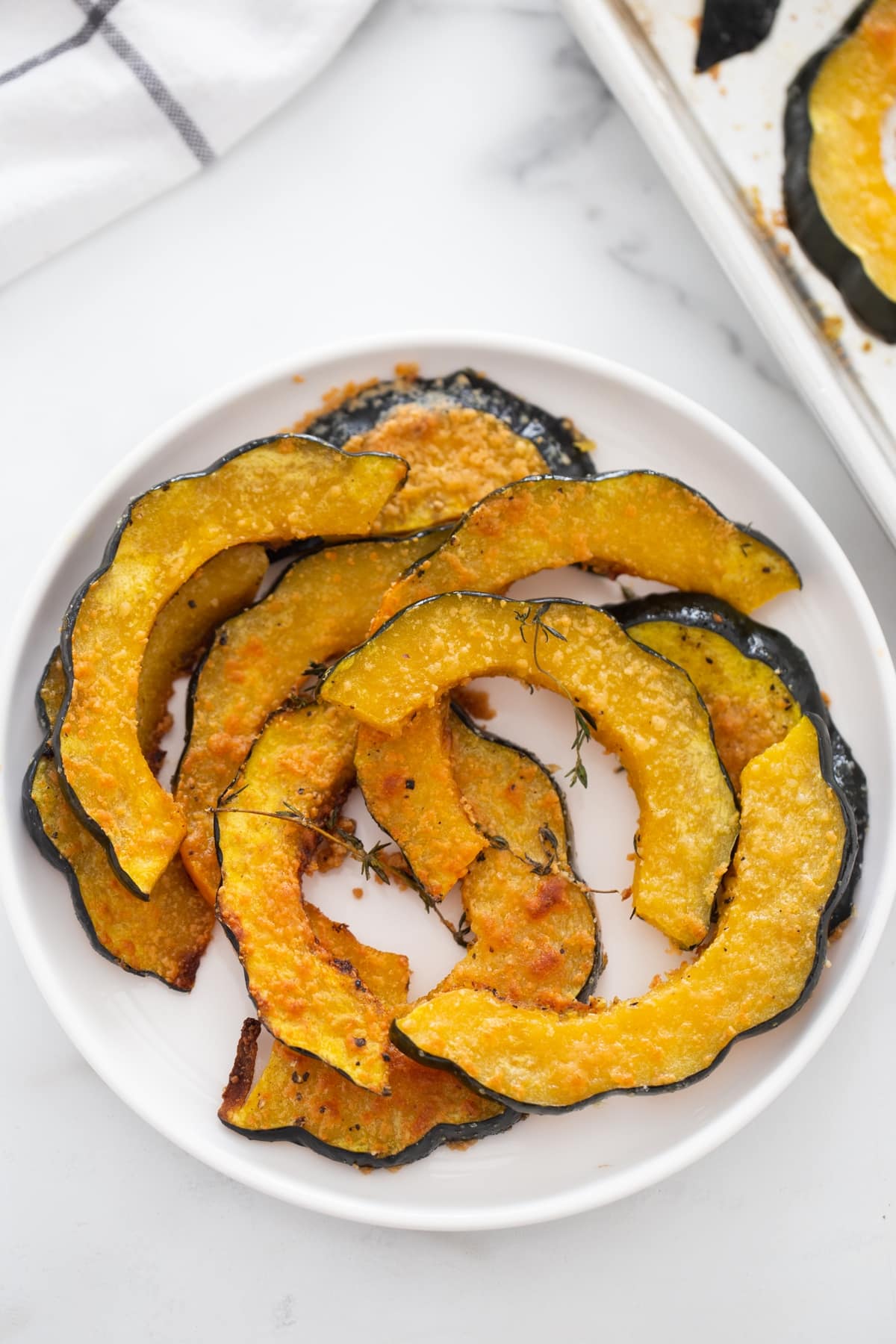 parmesan roasted acorn squash on a white plate with golden crispy edges and thyme