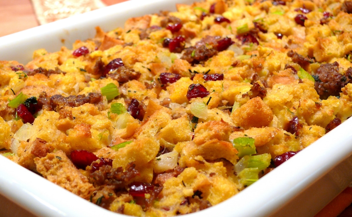 Side view of bread and sausage stuffing with cranberries in a white baking dish, showcasing its golden-brown crust and hearty texture.