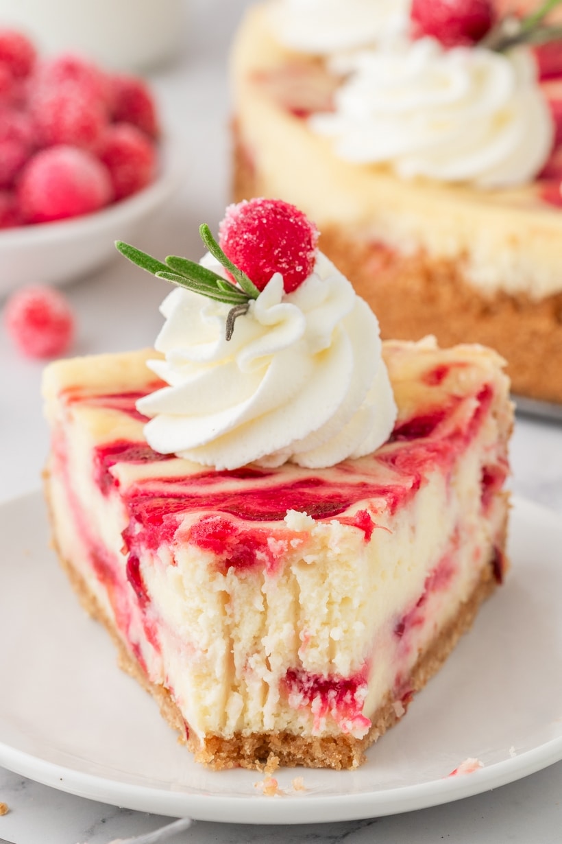 Slice of Cranberry Cheesecake with a Bite Taken. A single slice of cranberry cheesecake on a plate with a fork and a bite taken, showing the creamy filling and cranberry swirl.