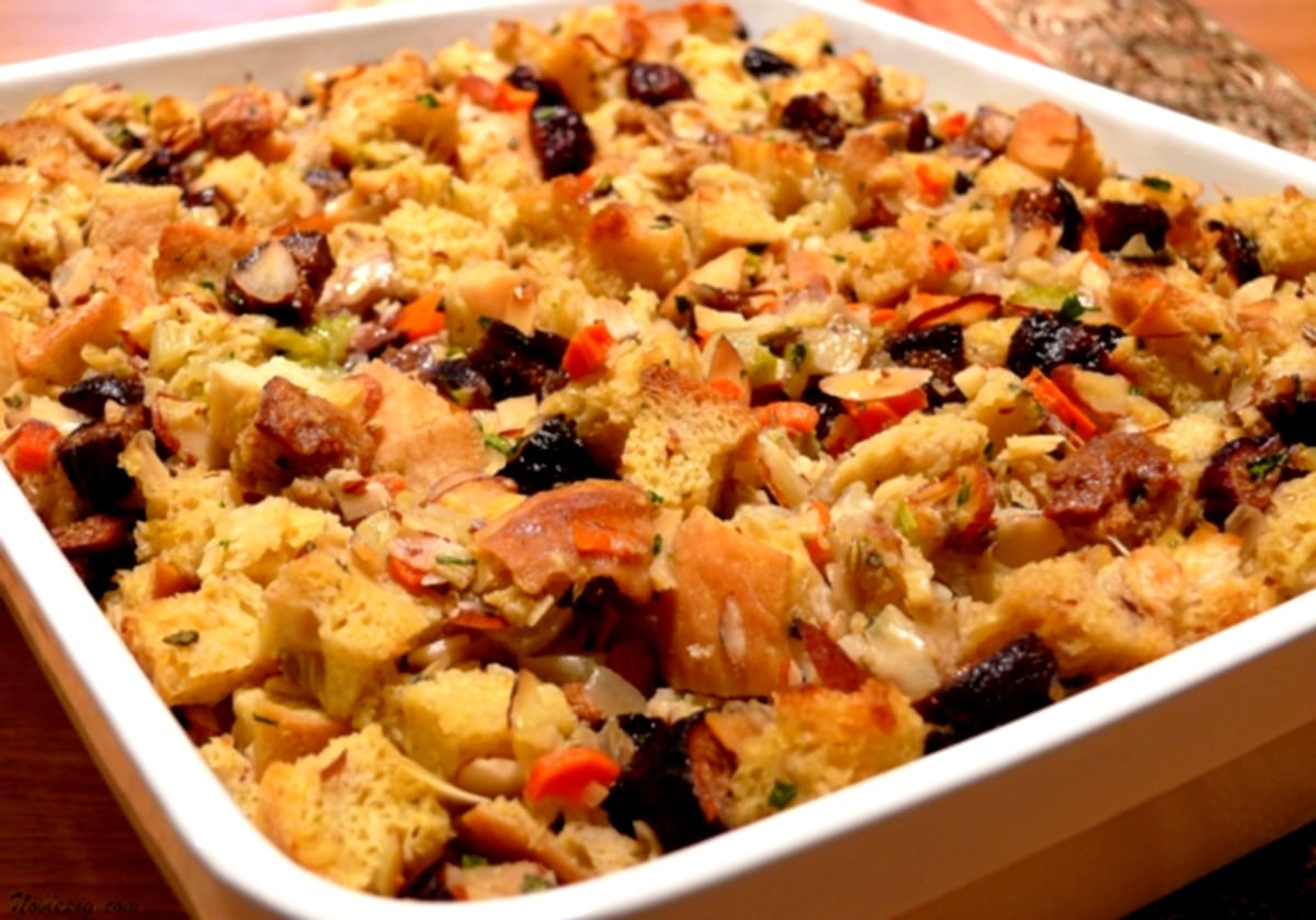 Overhead view of fig and almond stuffing with fennel in a white baking dish, showcasing its golden-brown crust and hearty texture.