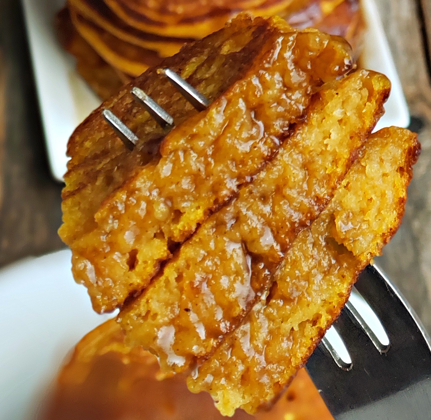 Close-up of fluffy pumpkin pancakes on a fork with cinnamon syrup soaking in.