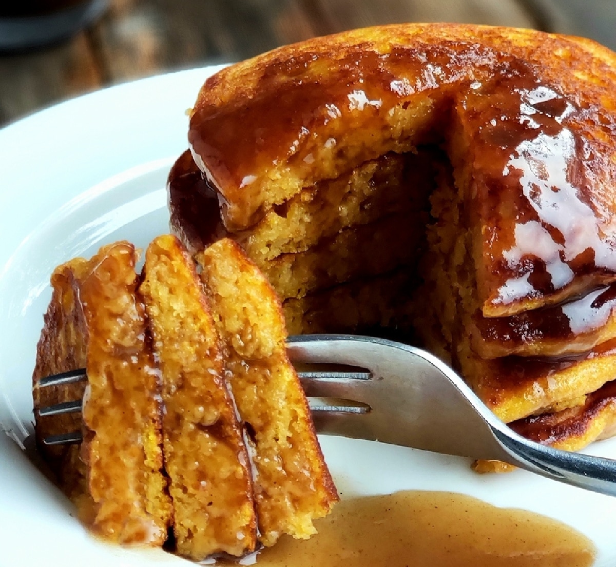 Stack of pumpkin pancakes on a plate with a cut slice dripping in cinnamon syrup.