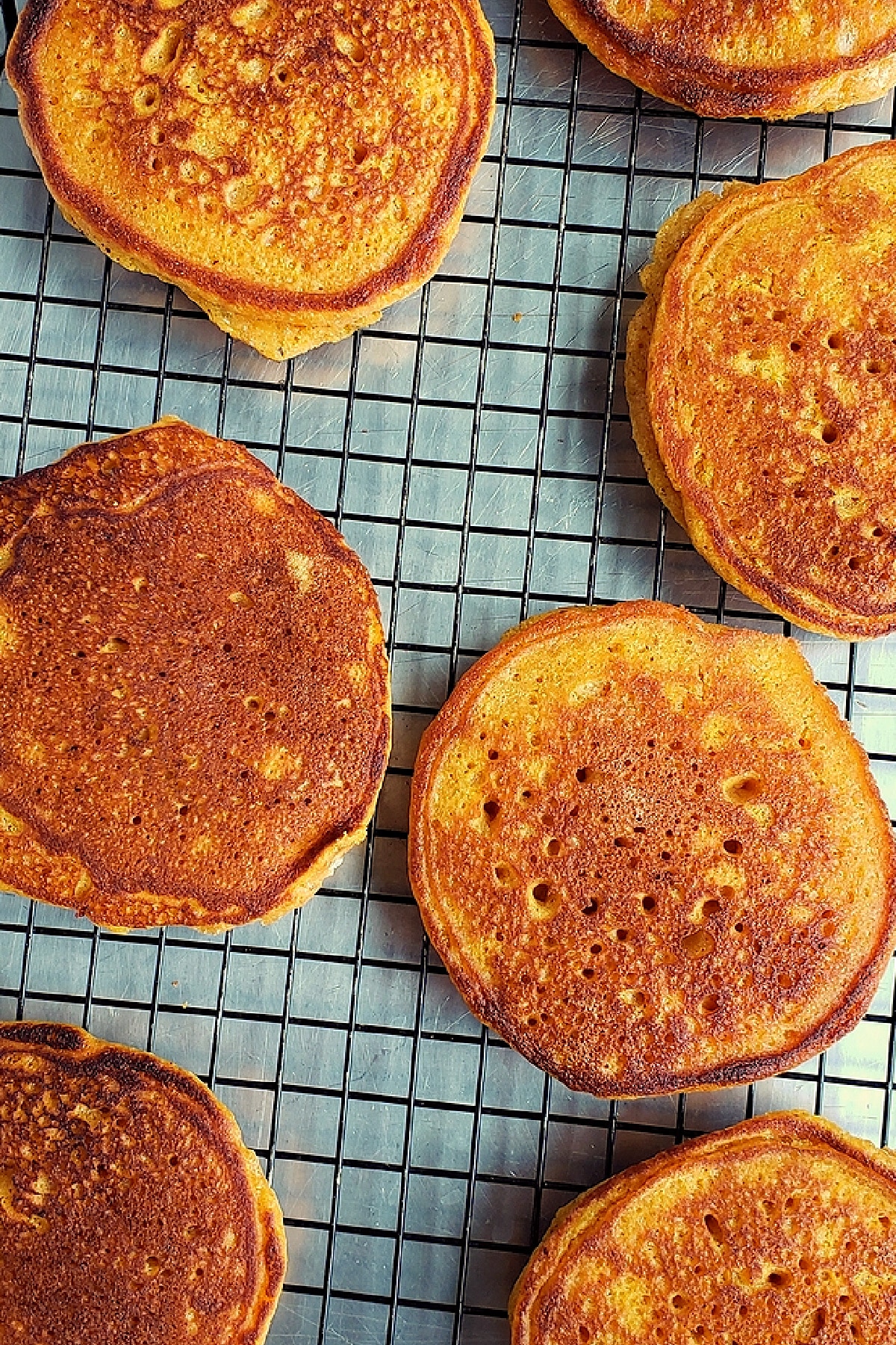 Pumpkin pancakes cooling on a wire rack after cooking.