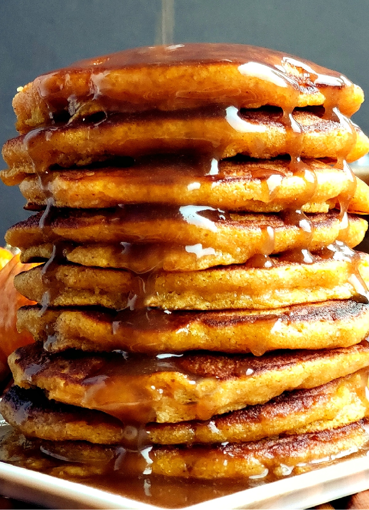 Tall stack of fluffy pumpkin pancakes with cinnamon syrup poured over the top.