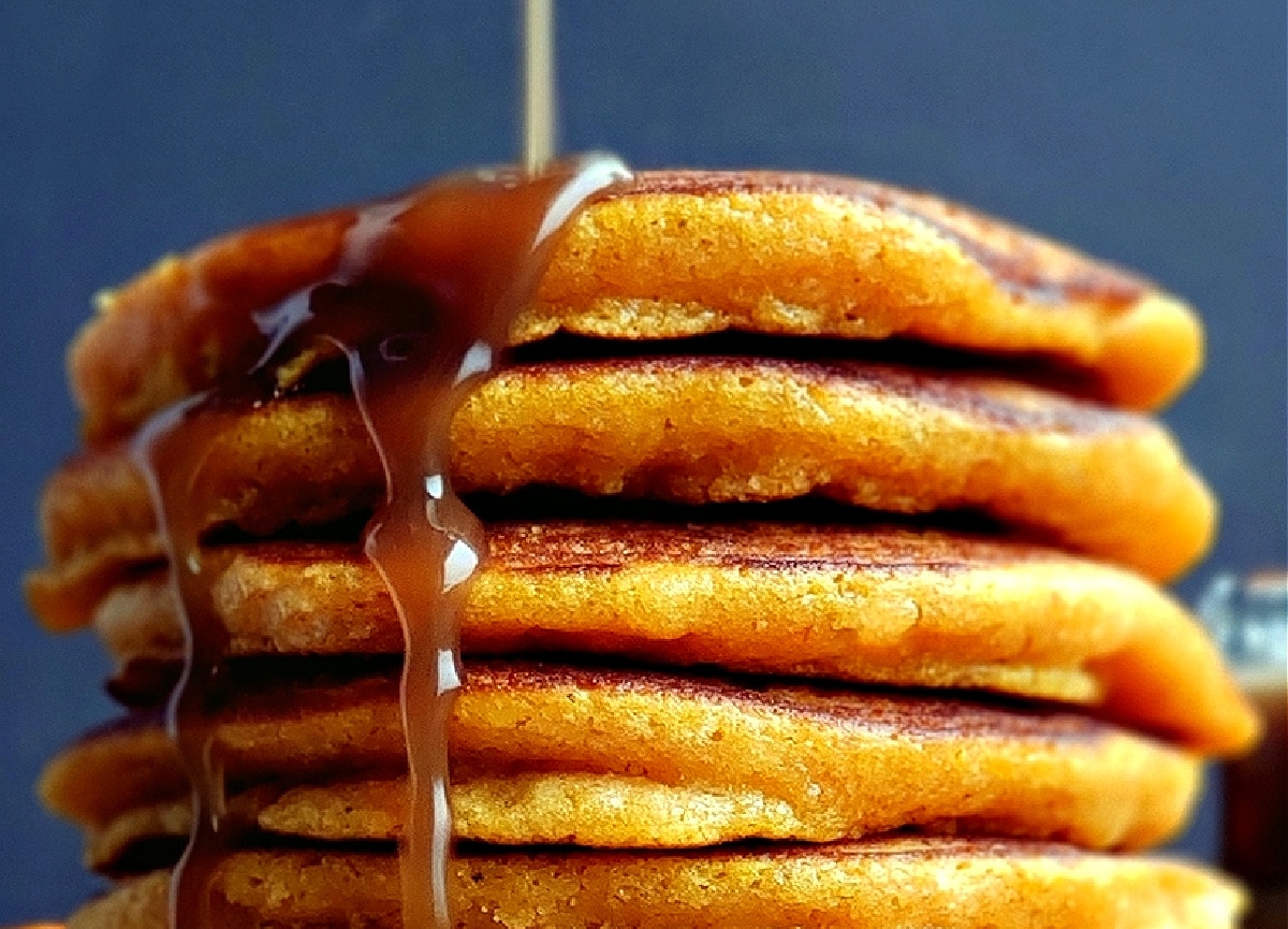 Cinnamon syrup being poured over a tall stack of pumpkin pancakes.