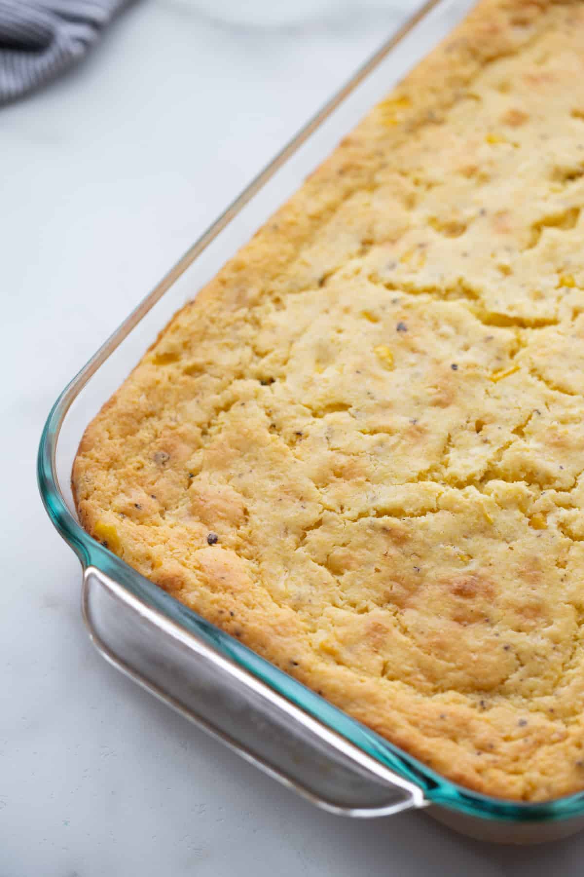 Freshly baked corn pudding in a 9x13-inch casserole dish, still warm and golden, before cinnamon is added.