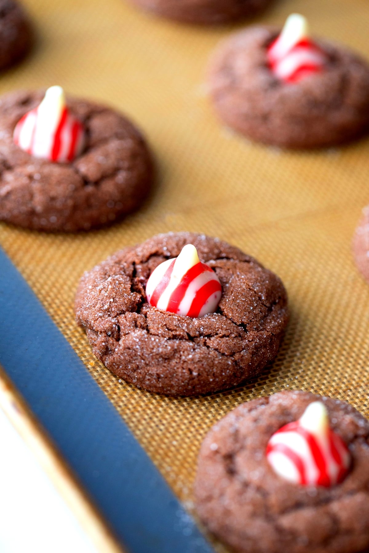 Baked Dark Chocolate Peppermint Crackle Cookies topped with a Hershey's Kiss, cooling on a silicone mat.