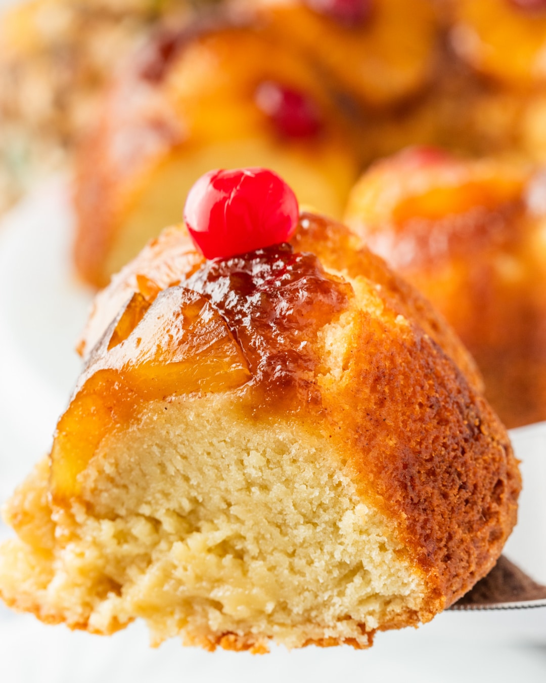 Slice of Pineapple Upside Down Cake with Cherry A single slice of pineapple upside down Bundt cake with golden edges and a cherry on top.