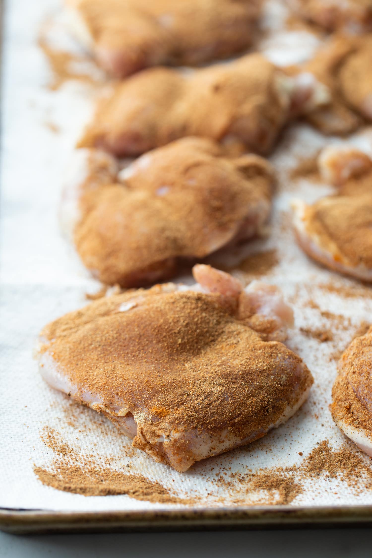 Raw chicken thighs on a baking sheet, evenly coated with the spice blend.