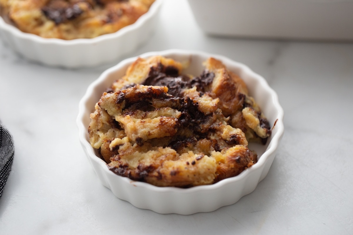 Chocolate Croissant Bread Pudding served A single serving of chocolate croissant bread pudding in a bowl, topped with a spoonful of melted chocolate and ready to be enjoyed.