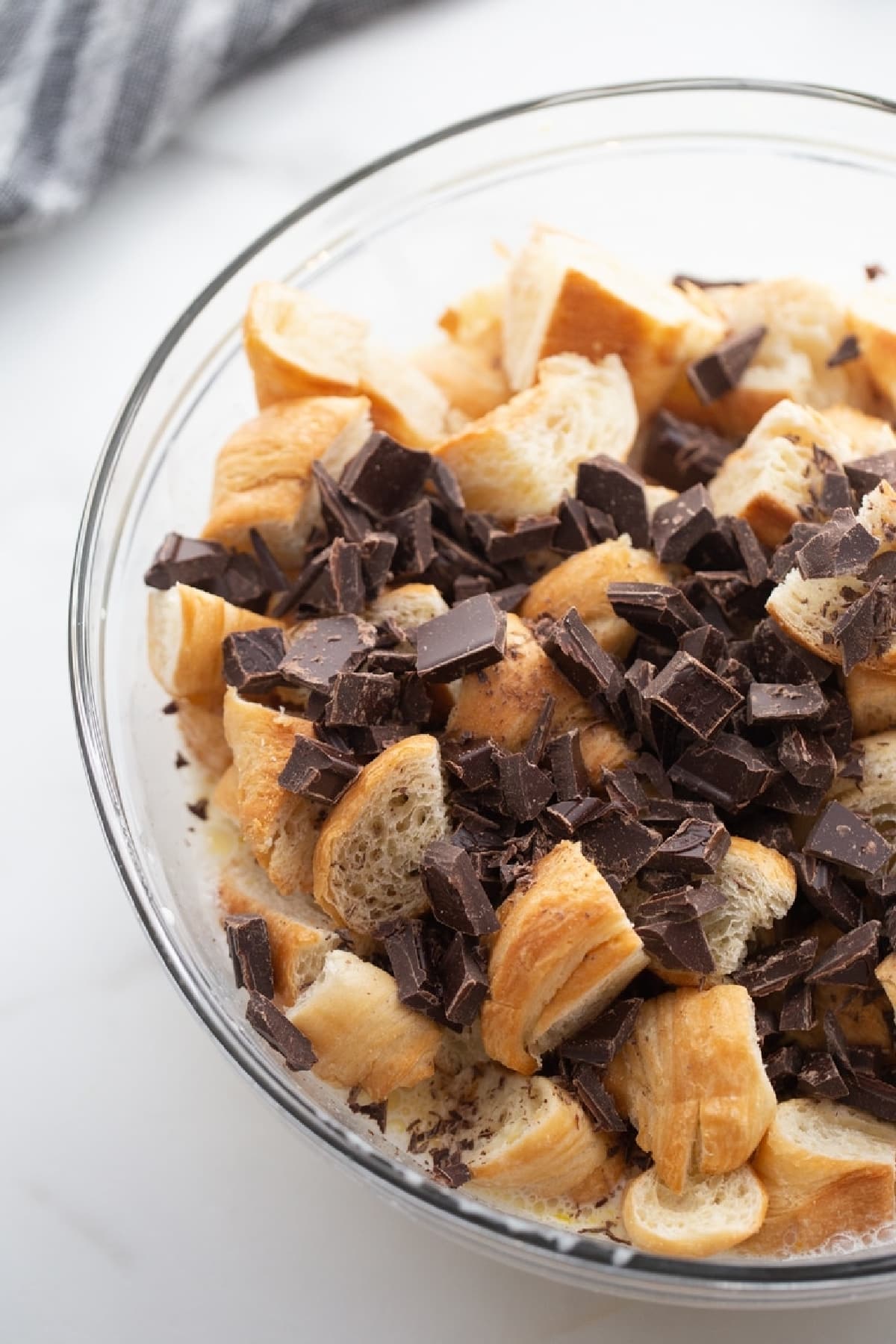 Chocolate Croissant Bread Pudding ingredients A bowl filled with torn croissant pieces and chunks of bittersweet chocolate, ready to be mixed with custard.