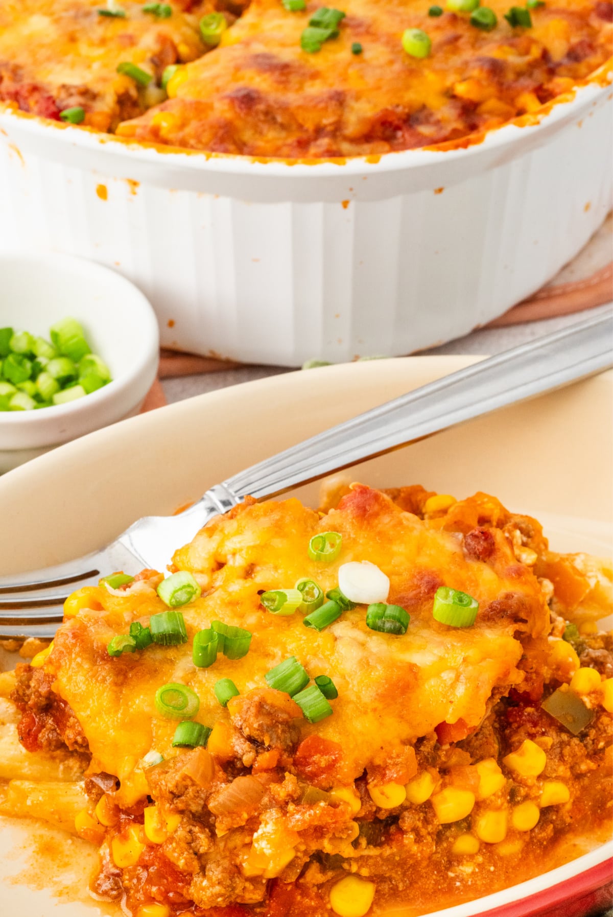Slice of easy ground beef casserole with pasta, corn, and melted cheddar cheese on a plate