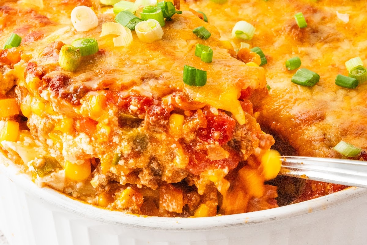Serving being scooped from baked ground beef casserole with corn, pasta, and cheddar
