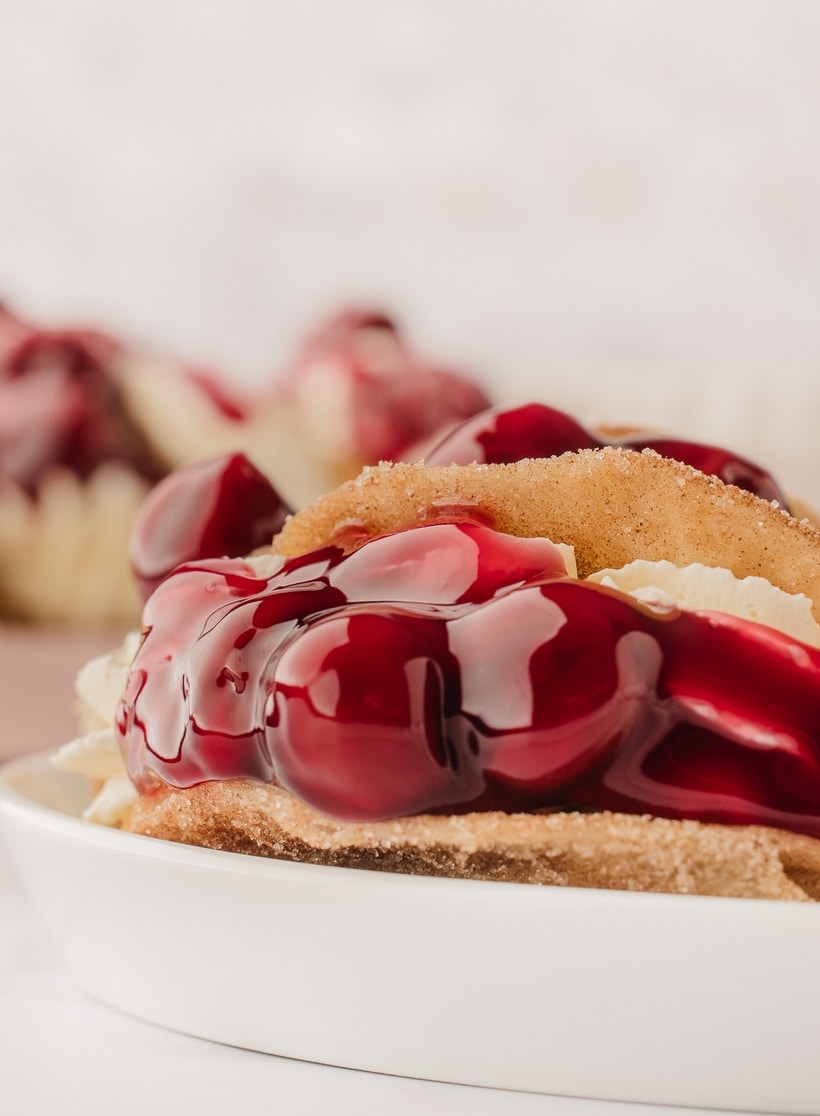Closeup of a single cherry cheesecake taco on its side, showcasing the creamy filling and cherry topping.