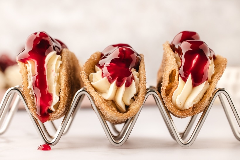 Three mini cherry cheesecake tacos in a taco holder, showcasing the crispy cinnamon-sugar shells and creamy cheesecake filling.