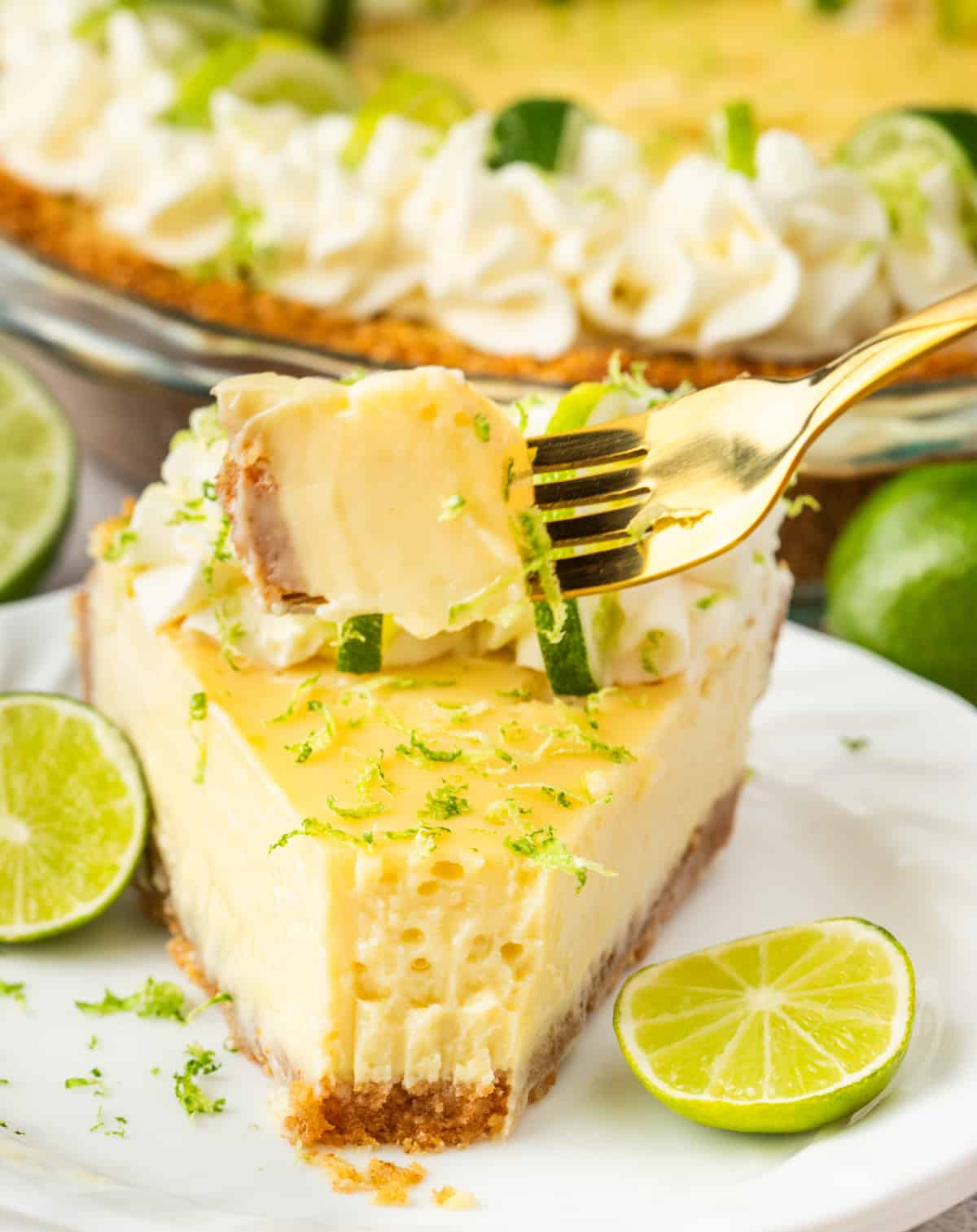 Forkful of key lime pie with slice behind Bite of key lime pie on a fork with the slice in the background