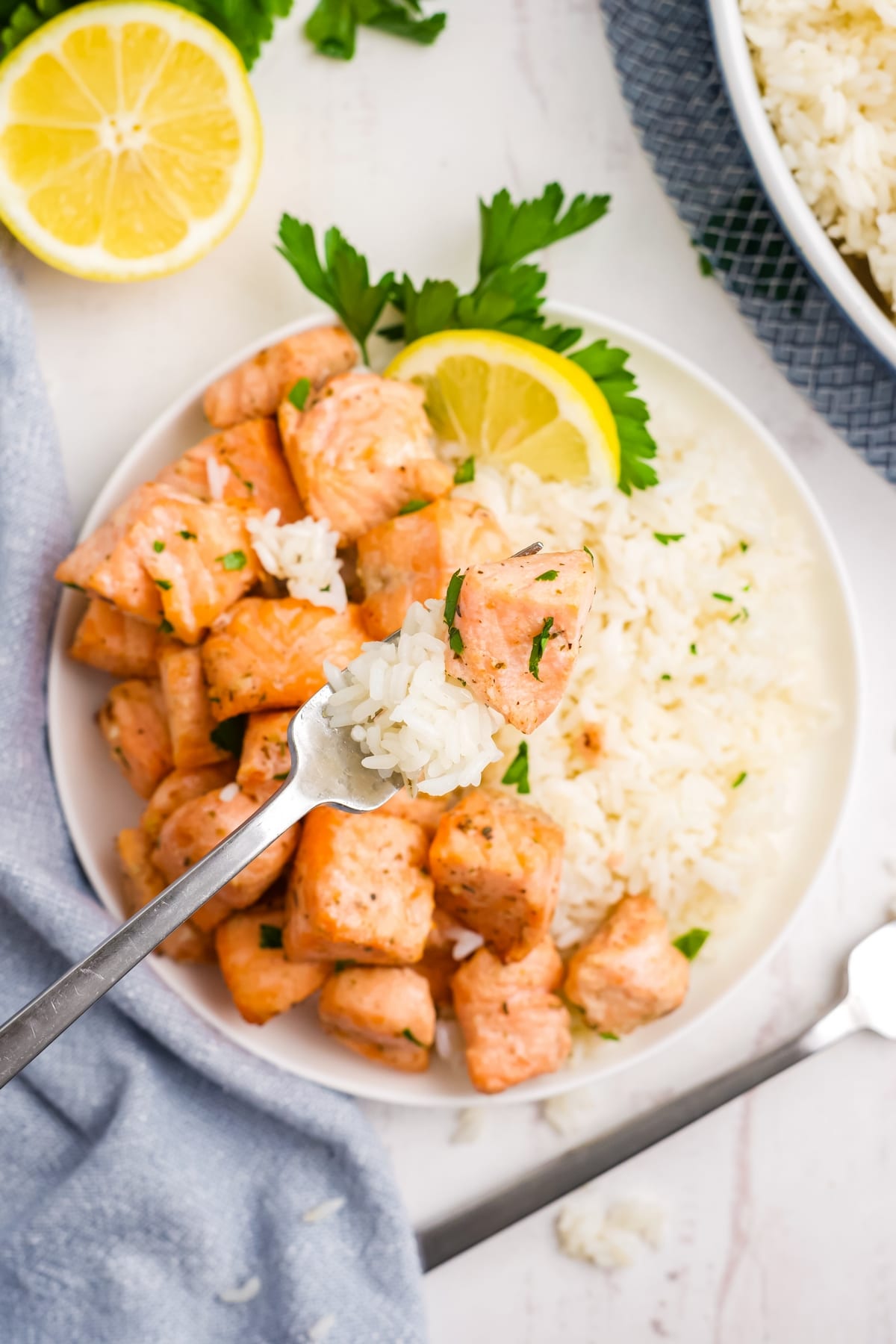 Try these mouthwatering air fryer salmon bites with lemon garlic butter sauce. Quick and easy, they make a perfect meal served over rice. air fryer salmon bites on a white plate with a fork