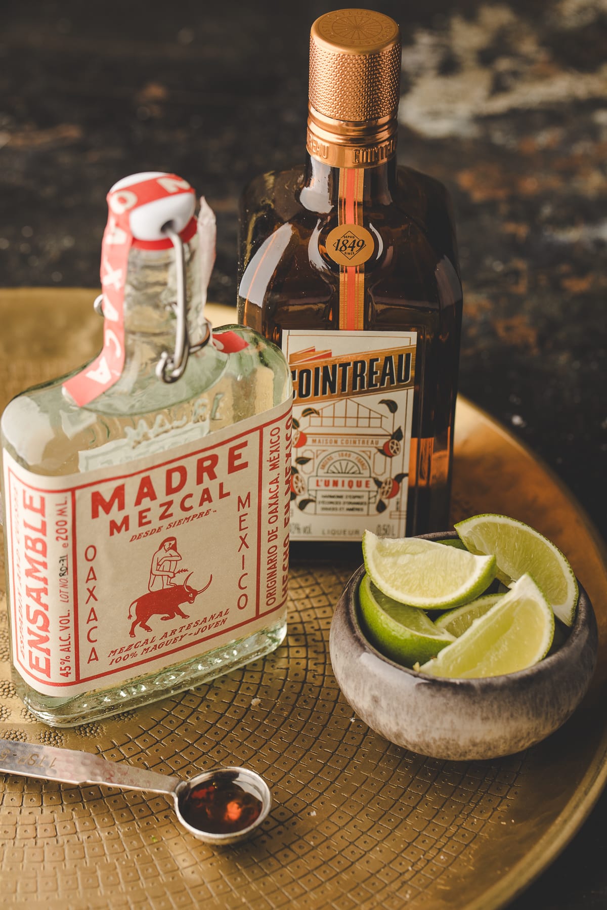 ingredients for mezcal margarita with mezcal, Cointreau, fresh lime wedges, and agave