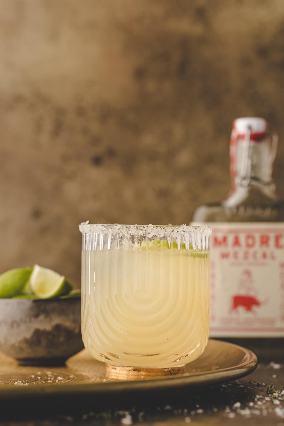 mezcal margarita recipe with salted rim in rocks glass with lime and mezcal bottle in background