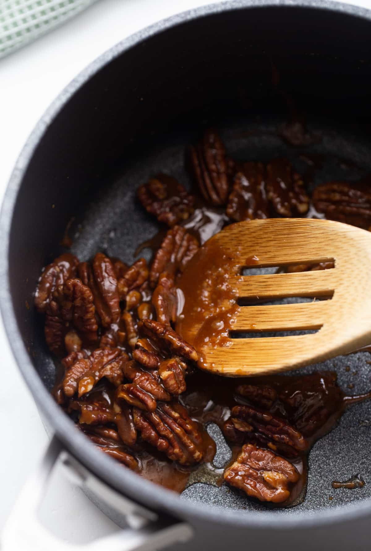 Pecan halves coated in brown sugar and butter, cooking in a small saucepan