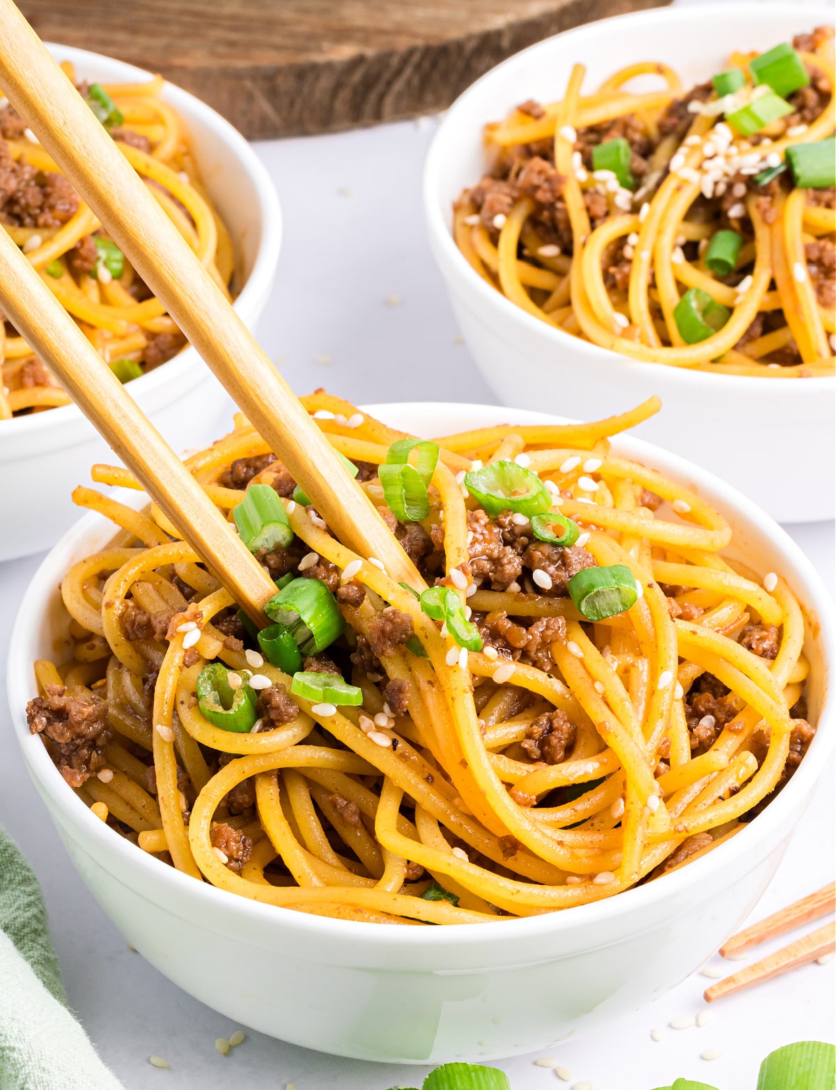 Mongolian beef with noodles coated in hoisin soy glaze, garnished with sesame seeds and green onions.