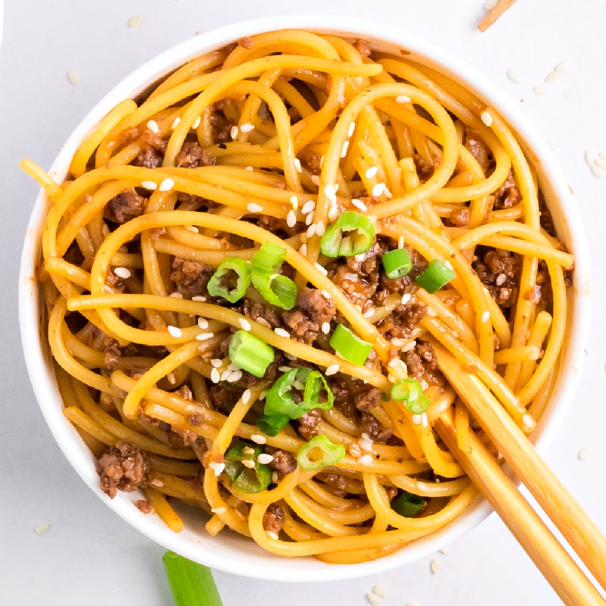 Easy Mongolian beef noodles with ground beef, sesame seeds, and green onions in a white bowl by Noble Pig.