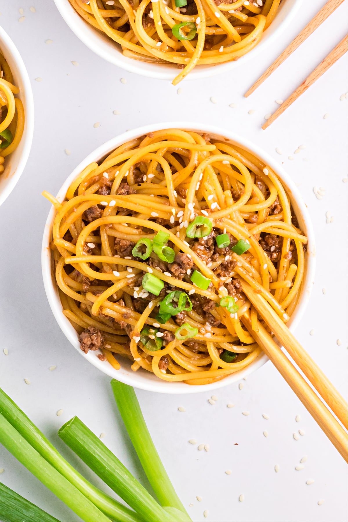 Easy Mongolian beef noodles recipe in a bowl with chopsticks, topped with sesame seeds and sliced green onions.