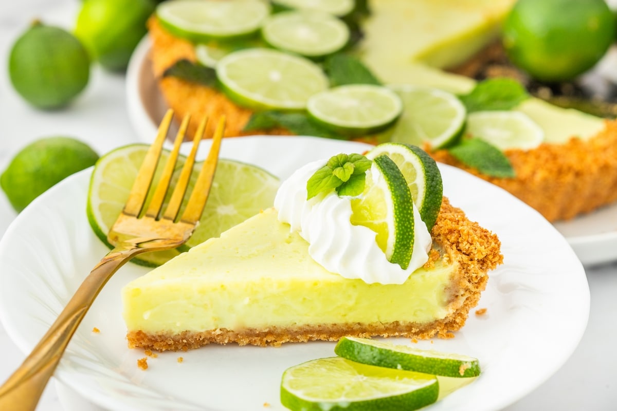 Slice of Key lime tart with whipped cream, lime, and mint garnish on top