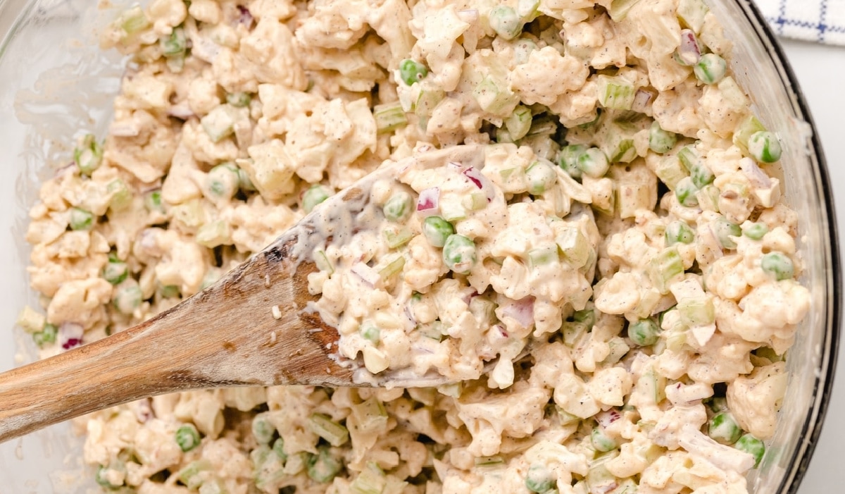 Cold creamy cauliflower salad ready to serve Overhead shot of cauliflower salad in a clear bowl with a wooden spoon