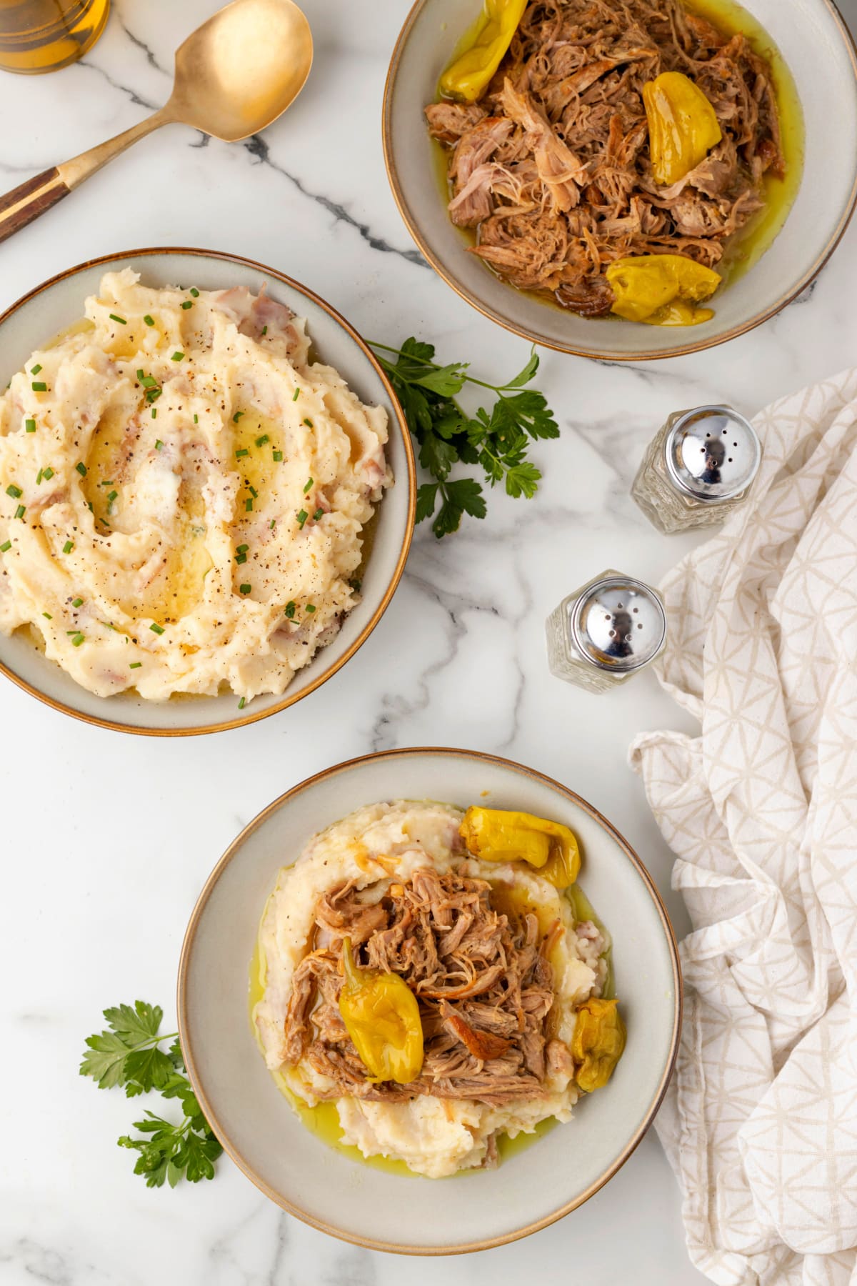Overhead dinner spread of Mississippi pork roast over mashed potatoes, with separate bowls of shredded pork and mashed potatoes.