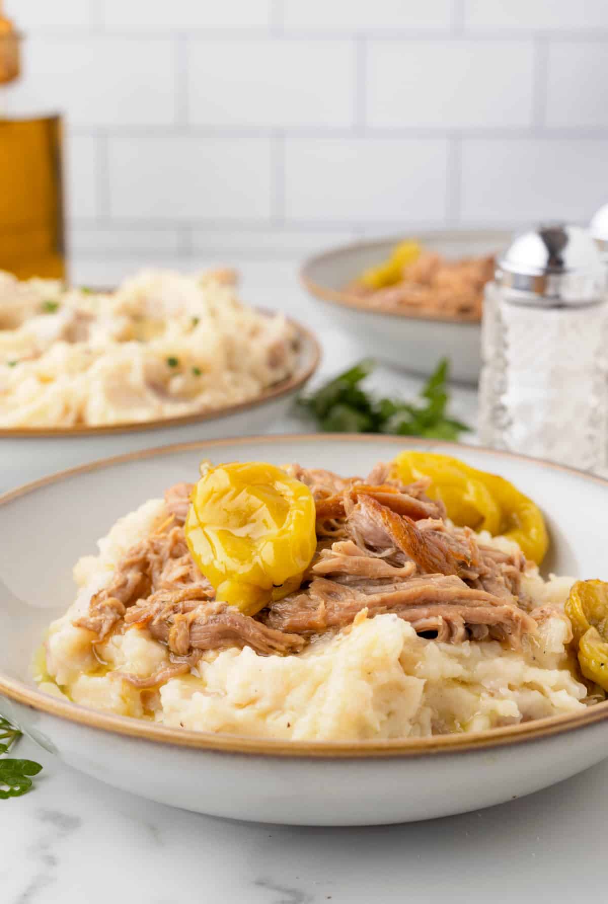Slow cooker Mississippi pork roast shredded over mashed potatoes with whole pepperoncini peppers and seasoned cooking liquid.