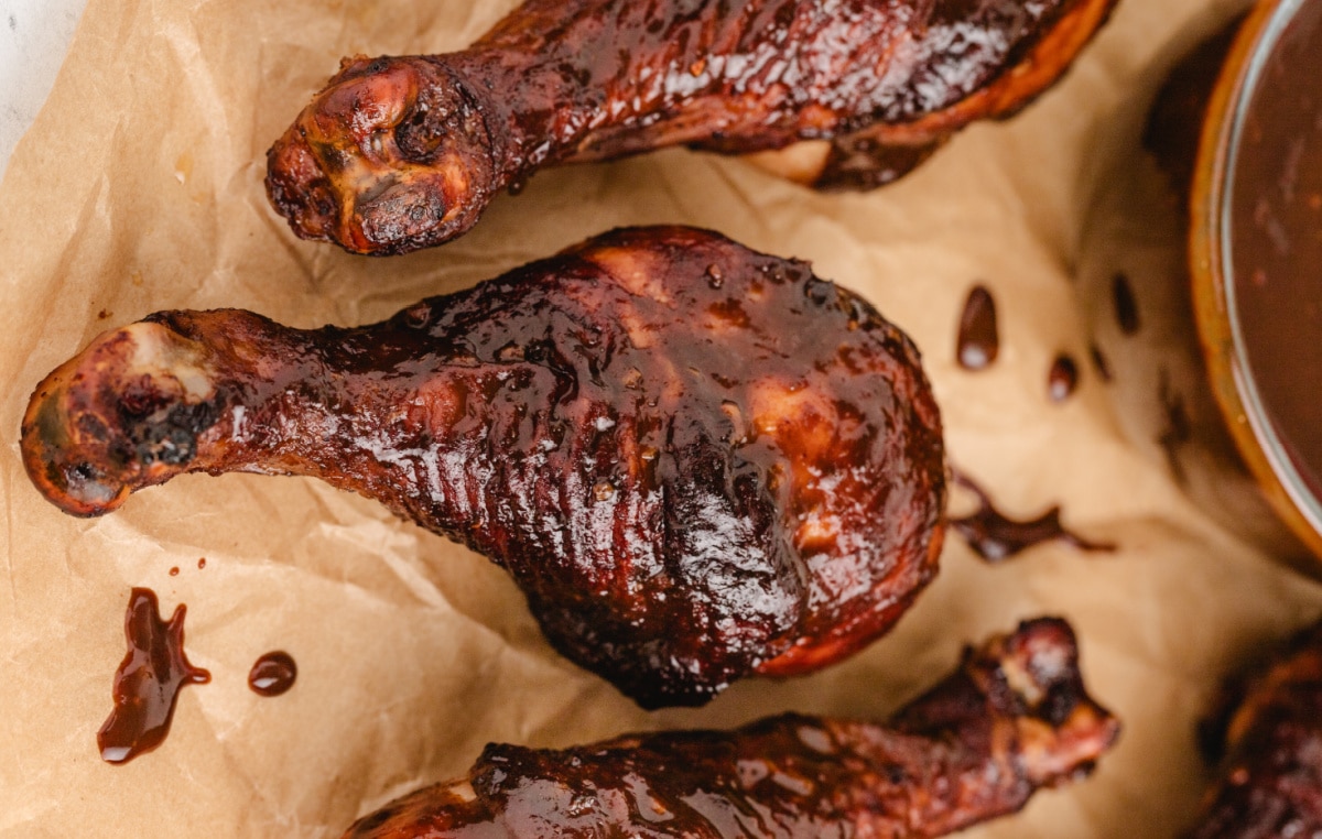 Three sticky chicken drumsticks resting on parchment paper