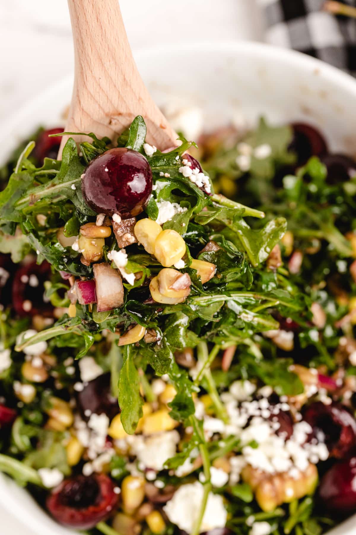 serving cherry corn salad with arugula and sweet cherries Wooden spoon lifting a serving of cherry corn salad with arugula, feta, corn, and red onion.
