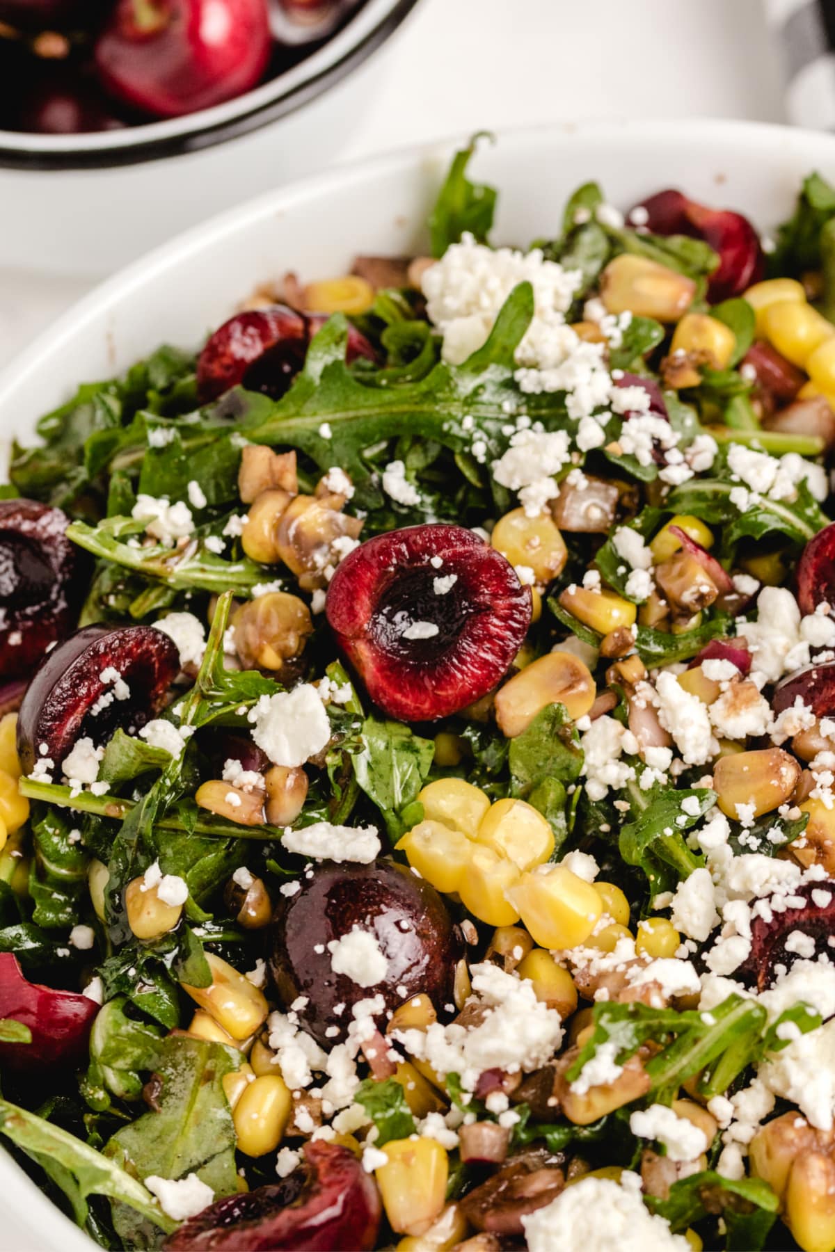 fresh cherry corn salad close up with feta Close-up of cherry corn salad showing halved cherries, arugula, grilled corn, and crumbled feta.
