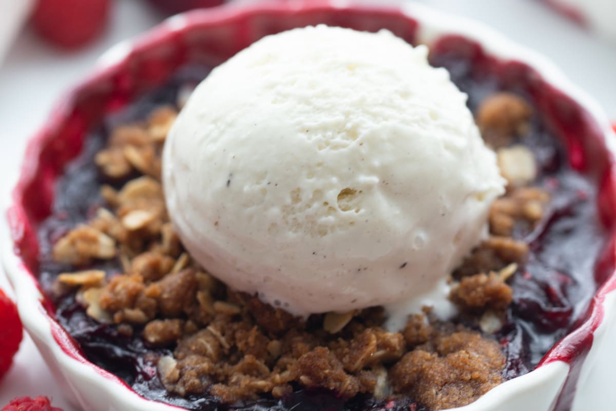 Vanilla ice cream melting over warm cherry berry crisp with oat topping in a ramekin.
