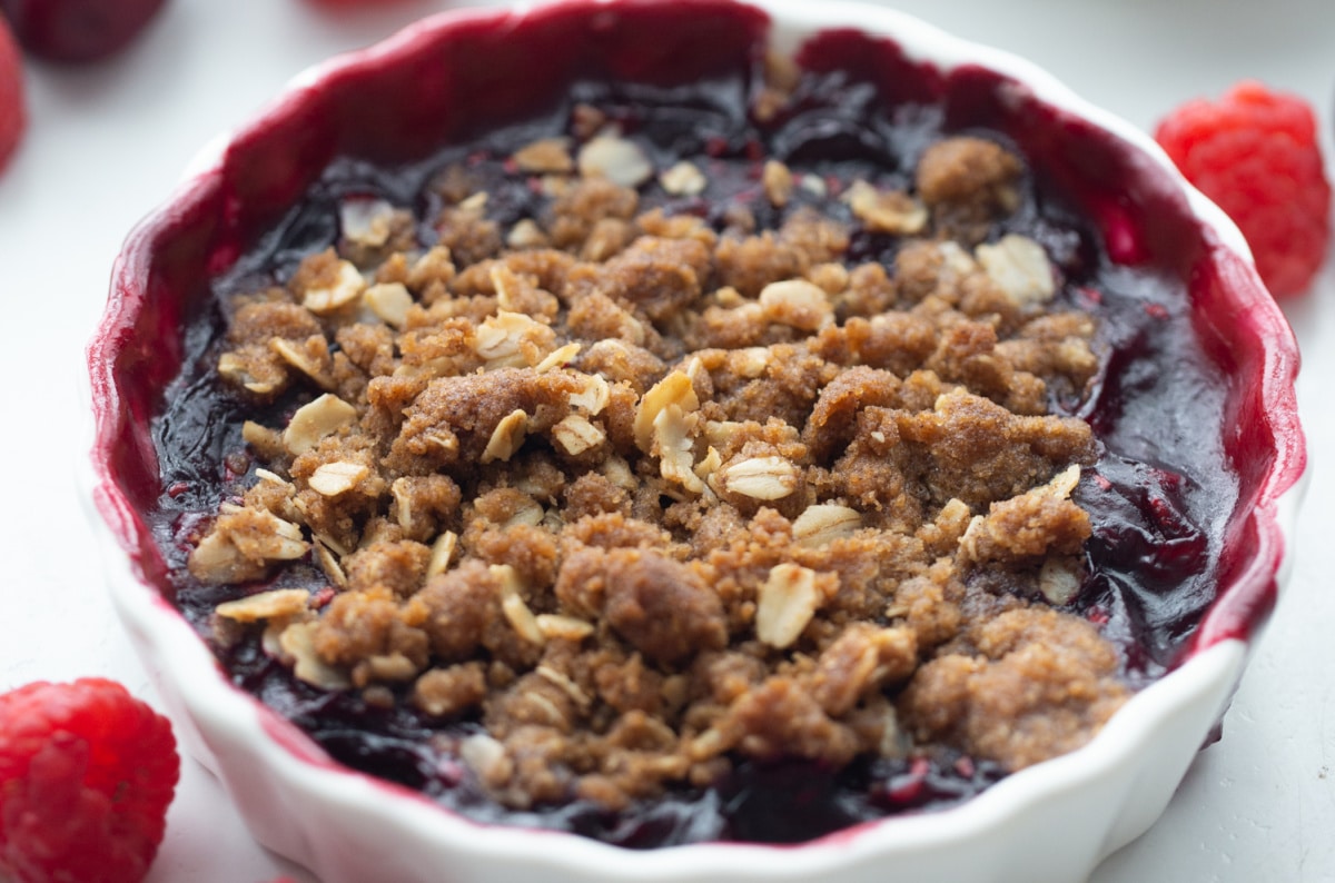 Close-up of golden oat topping on baked cherry raspberry crisp in a white ramekin. 