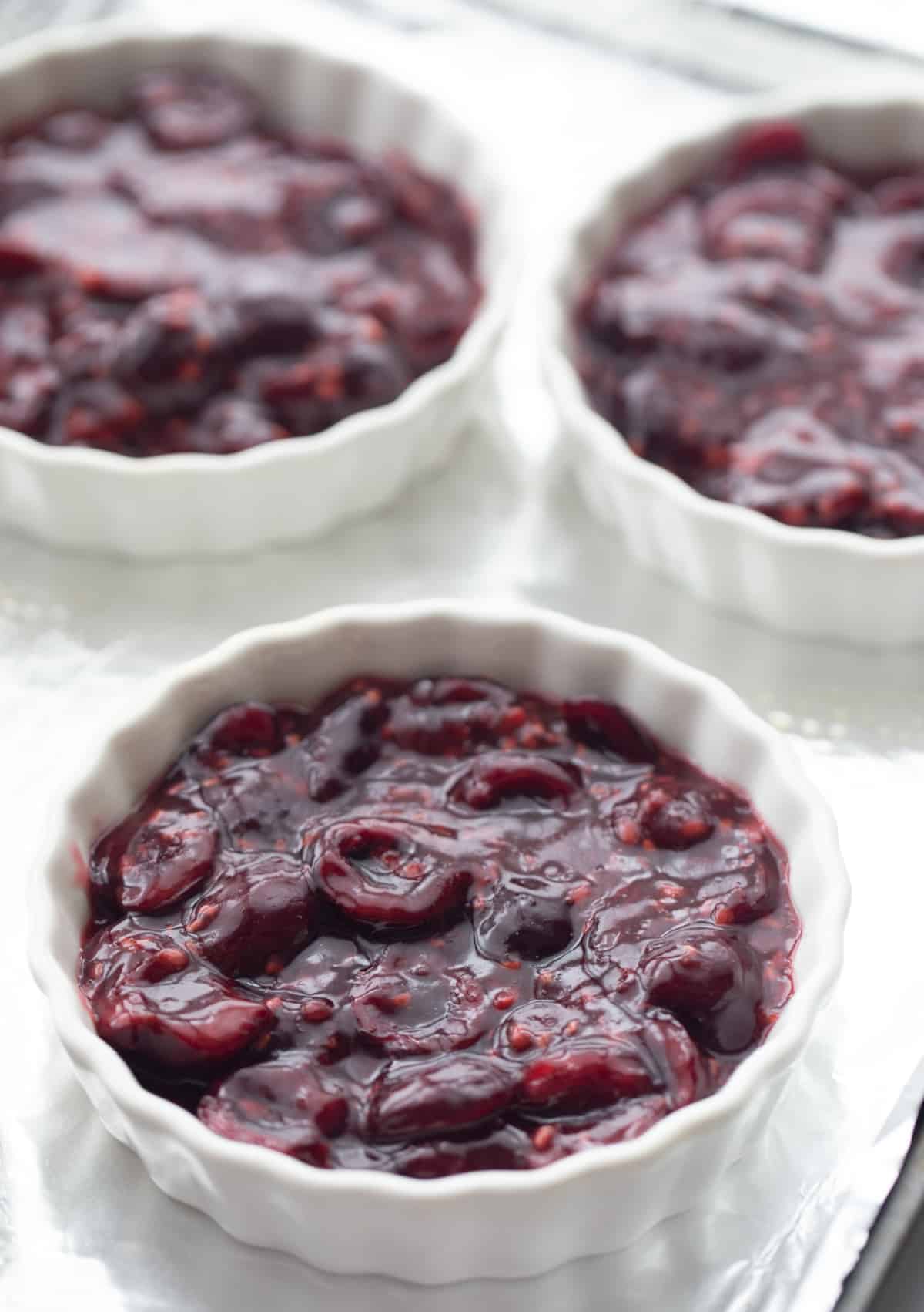 Cherry and raspberry crisp filling portioned into ramekins, ready for oat topping and baking.