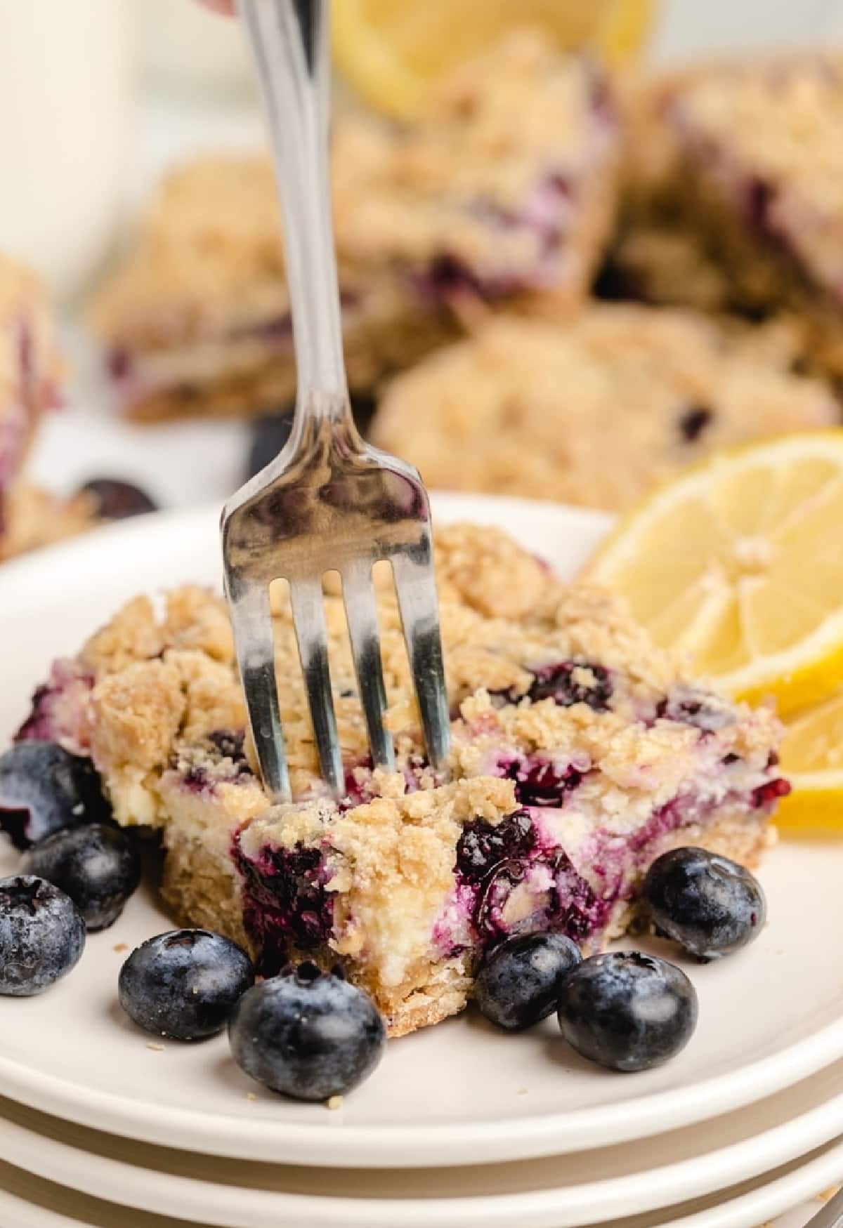 Fork cutting into a lemon blueberry crumble bar on a white plate