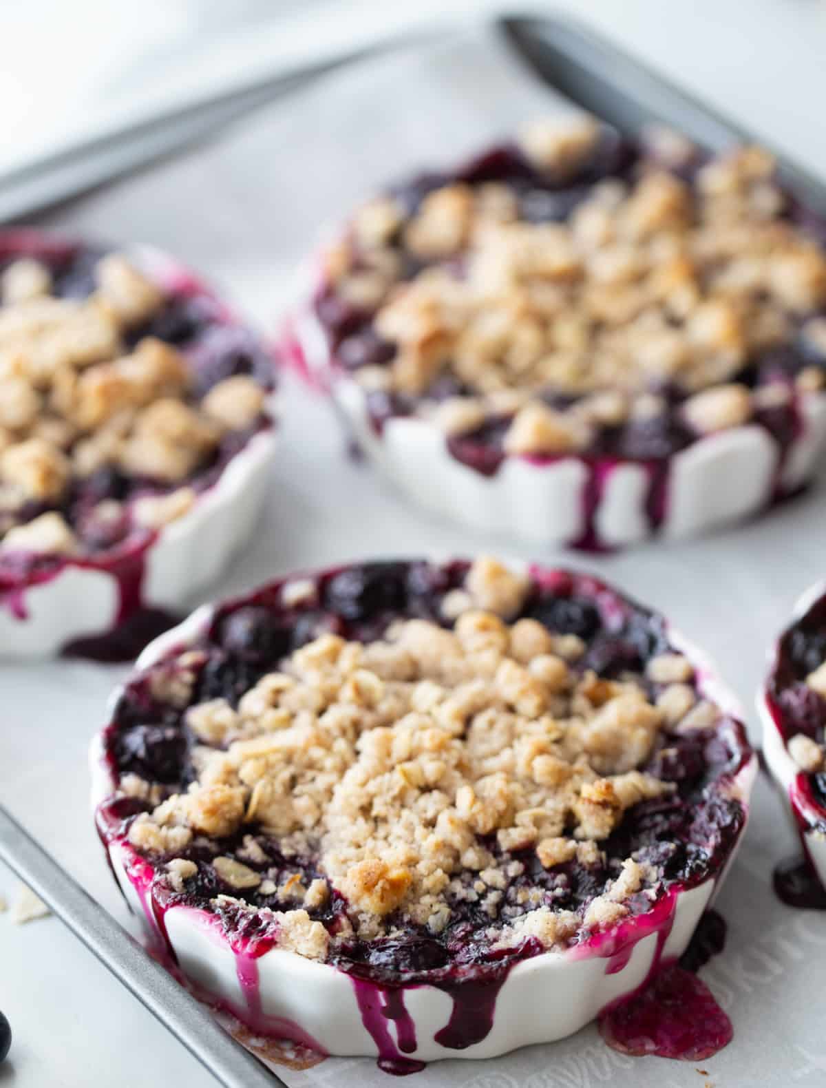 blueberry crisp after baking with filling overflow Baked blueberry crisps in ramekins with fruit bubbling over onto baking sheet