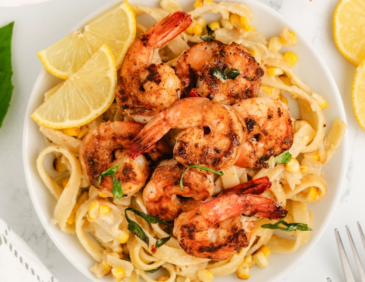 Bowl of blackened shrimp fettuccine with corn and lemon slices.