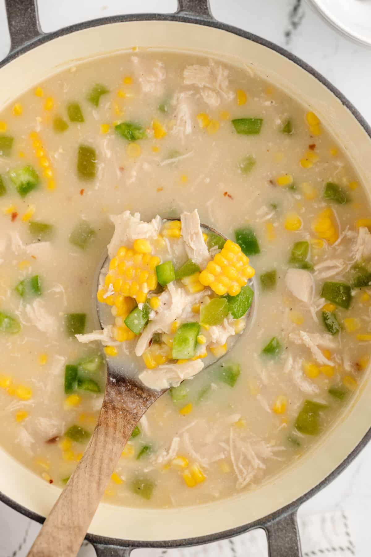 Chicken corn chowder in a Dutch oven with shredded chicken, fresh sweet corn, and green bell peppers.